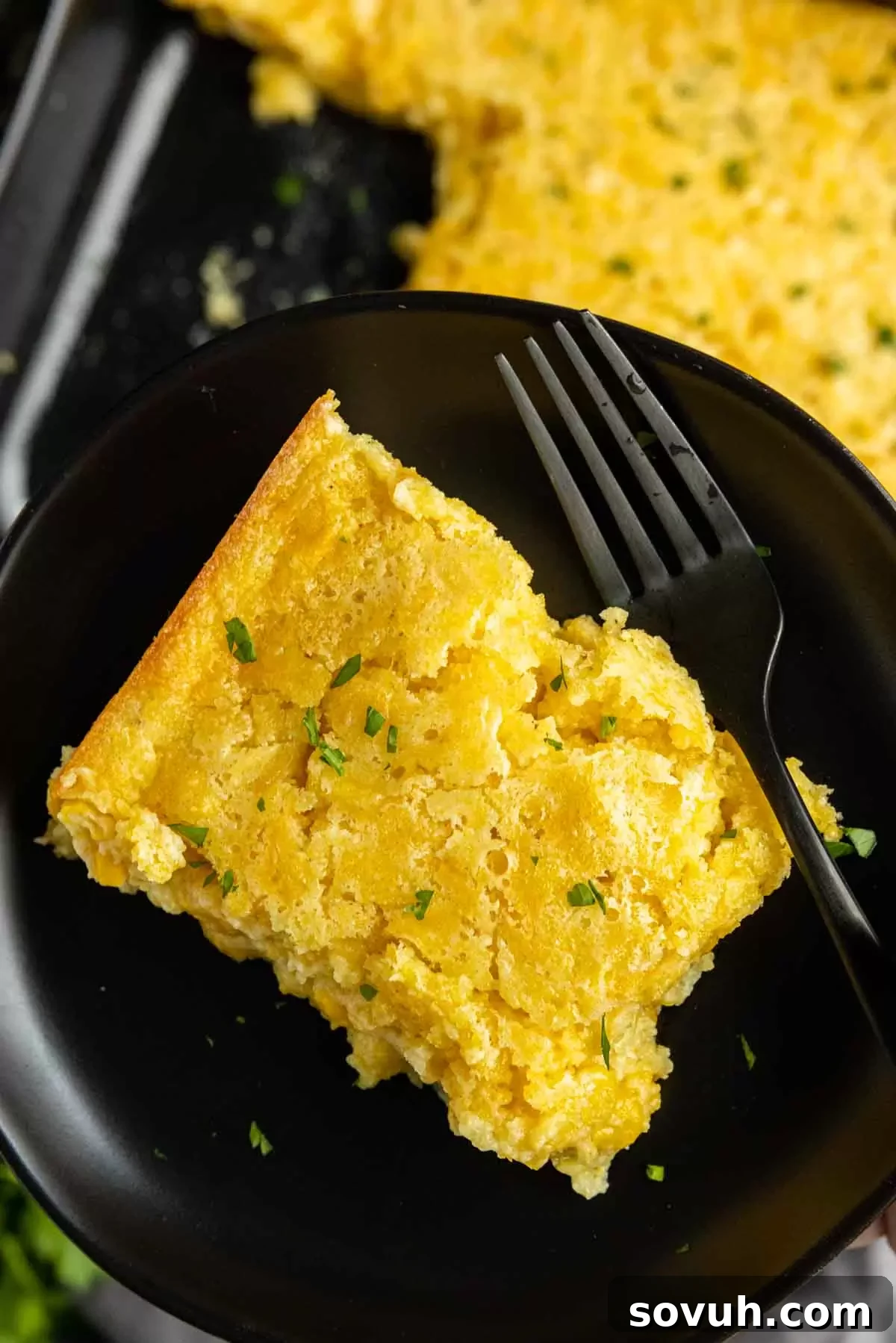 holding a plate of Creamed Corn Casserole with fork
