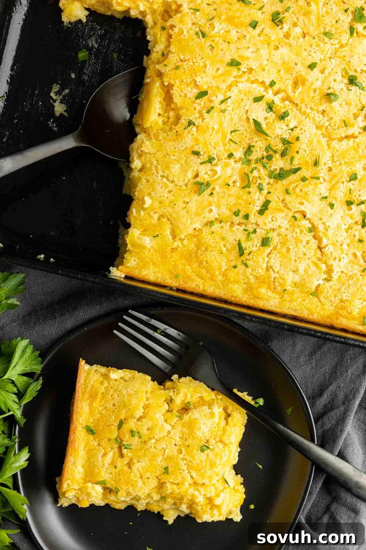 Creamed Corn Casserole on a black plate with black fork and casserole pan with spoon