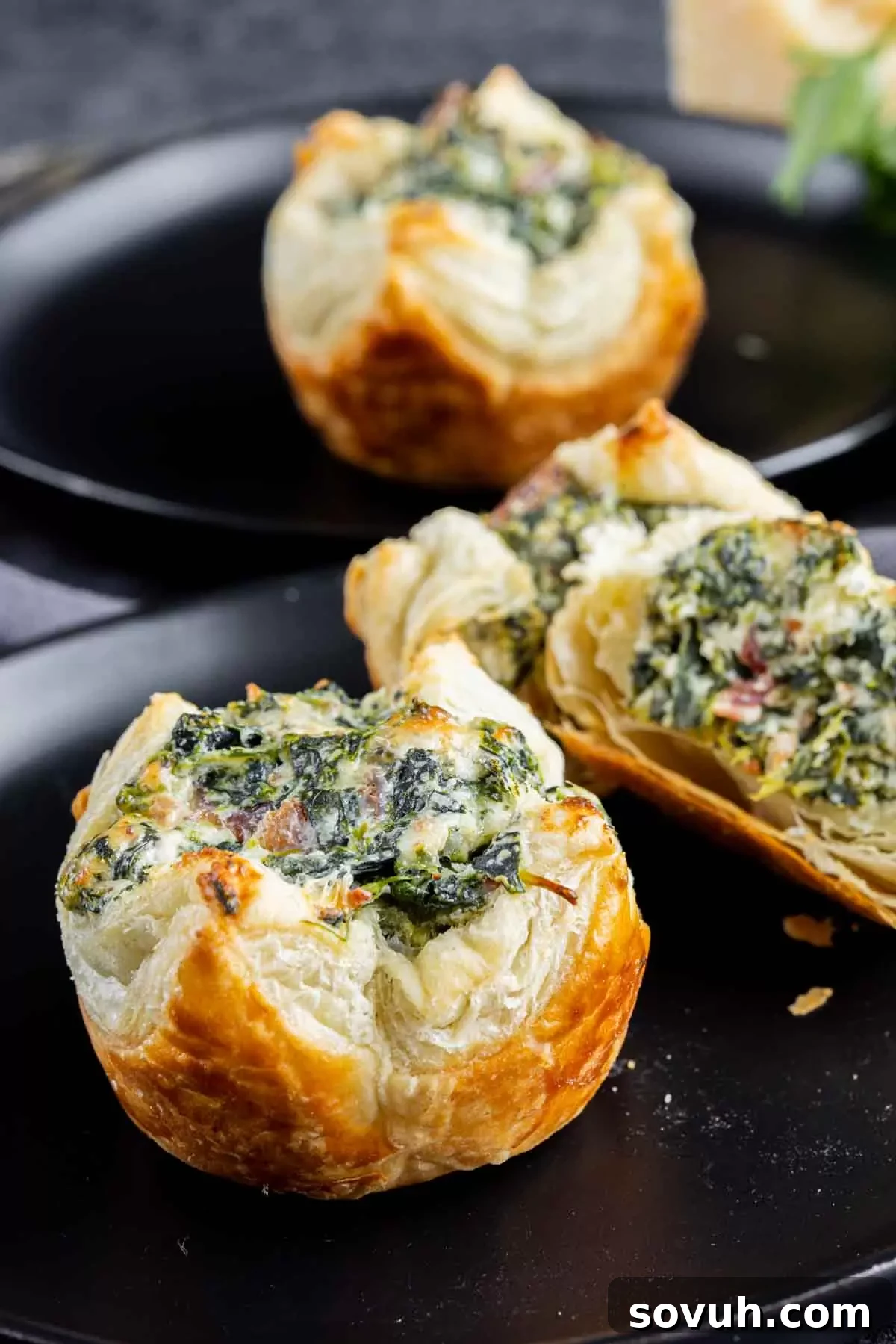 Freshly baked spinach puff pastry bites elegantly arranged on a black plate, showcasing their golden crust and enticing filling.