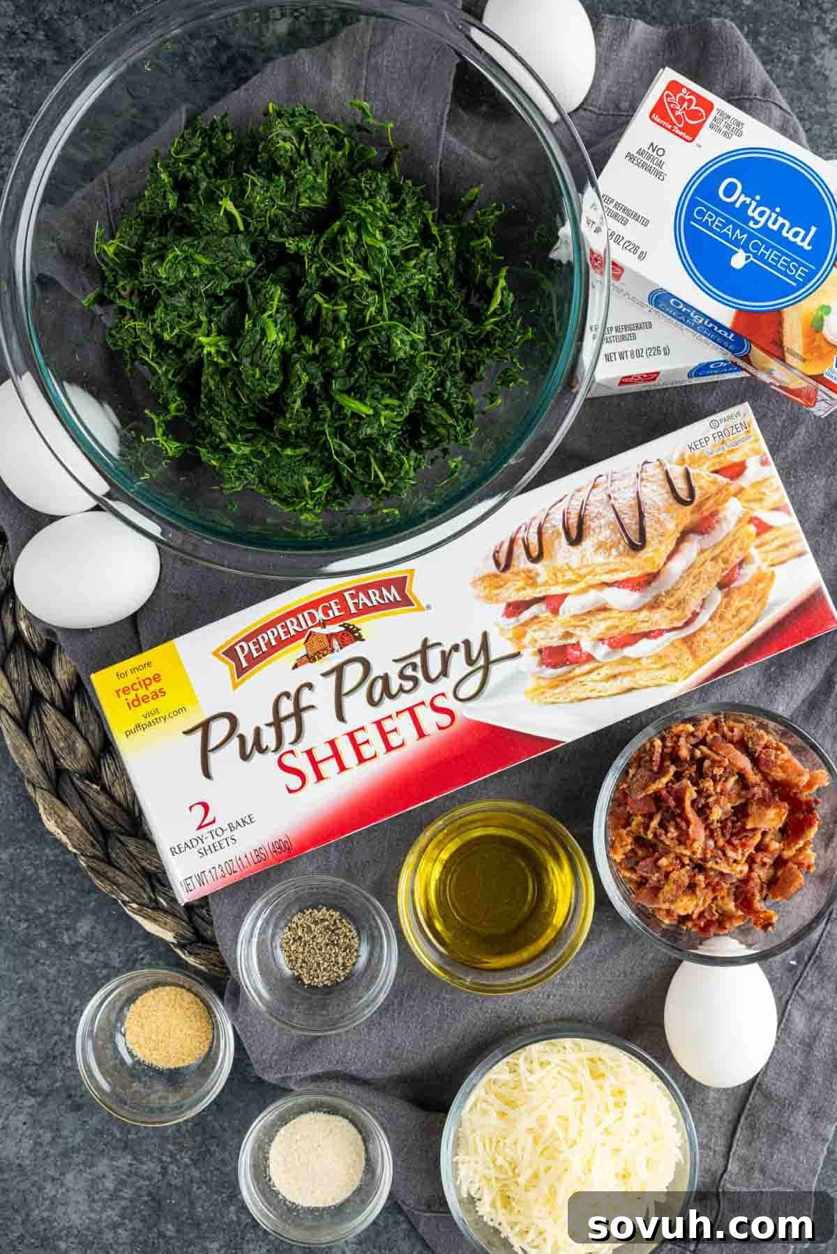 A selection of fresh ingredients laid out, including thawed puff pastry sheets, vibrant spinach, eggs, and various cheeses, ready for making delicious spinach puffs.
