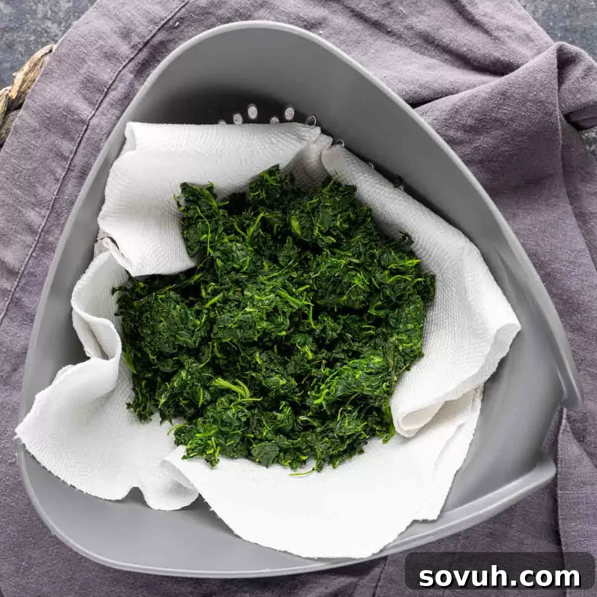 Thawed spinach in a strainer, being squeezed to remove excess water for the puff pastry filling.