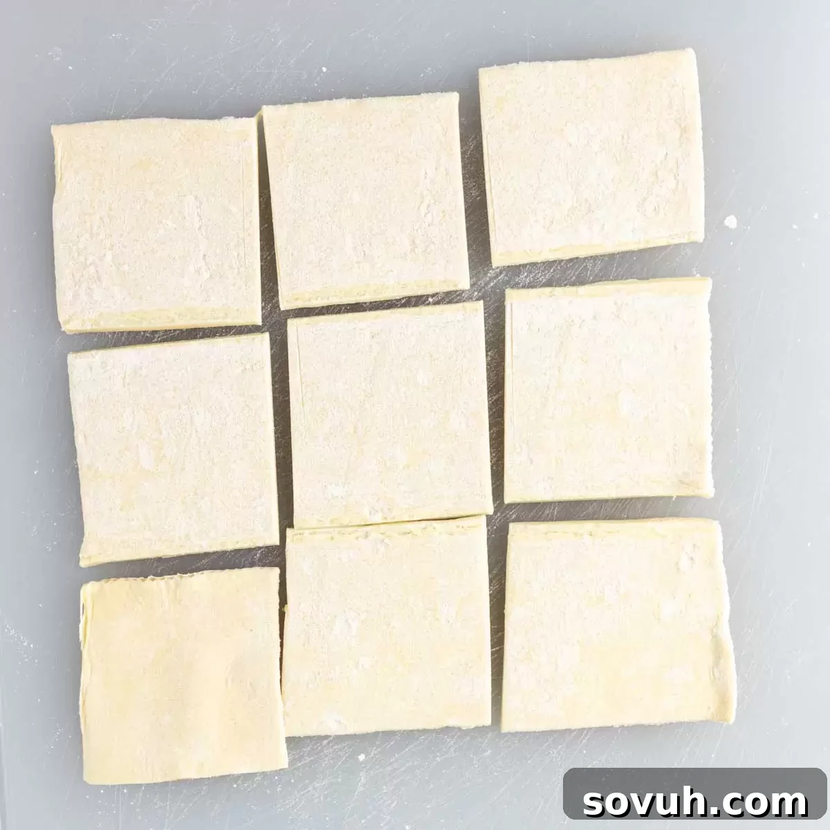 Thawed puff pastry sheets neatly cut into nine squares each, arranged on a lightly floured cutting board.