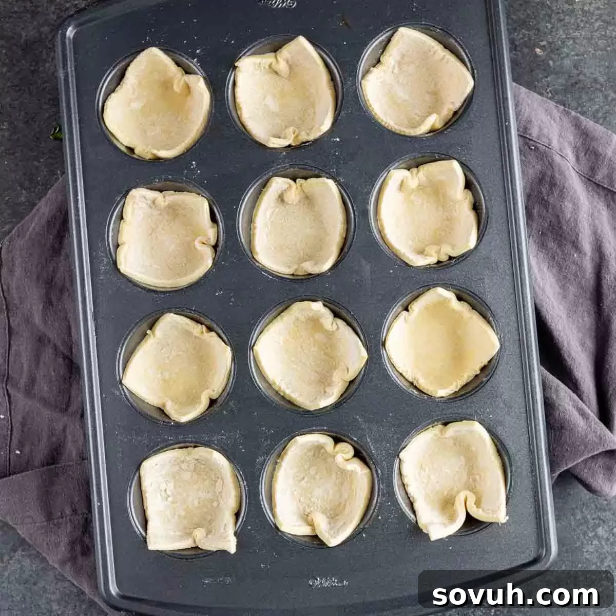 Individual squares of puff pastry gently pressed into the cups of a muffin tin, forming perfect bases for the spinach puff filling.