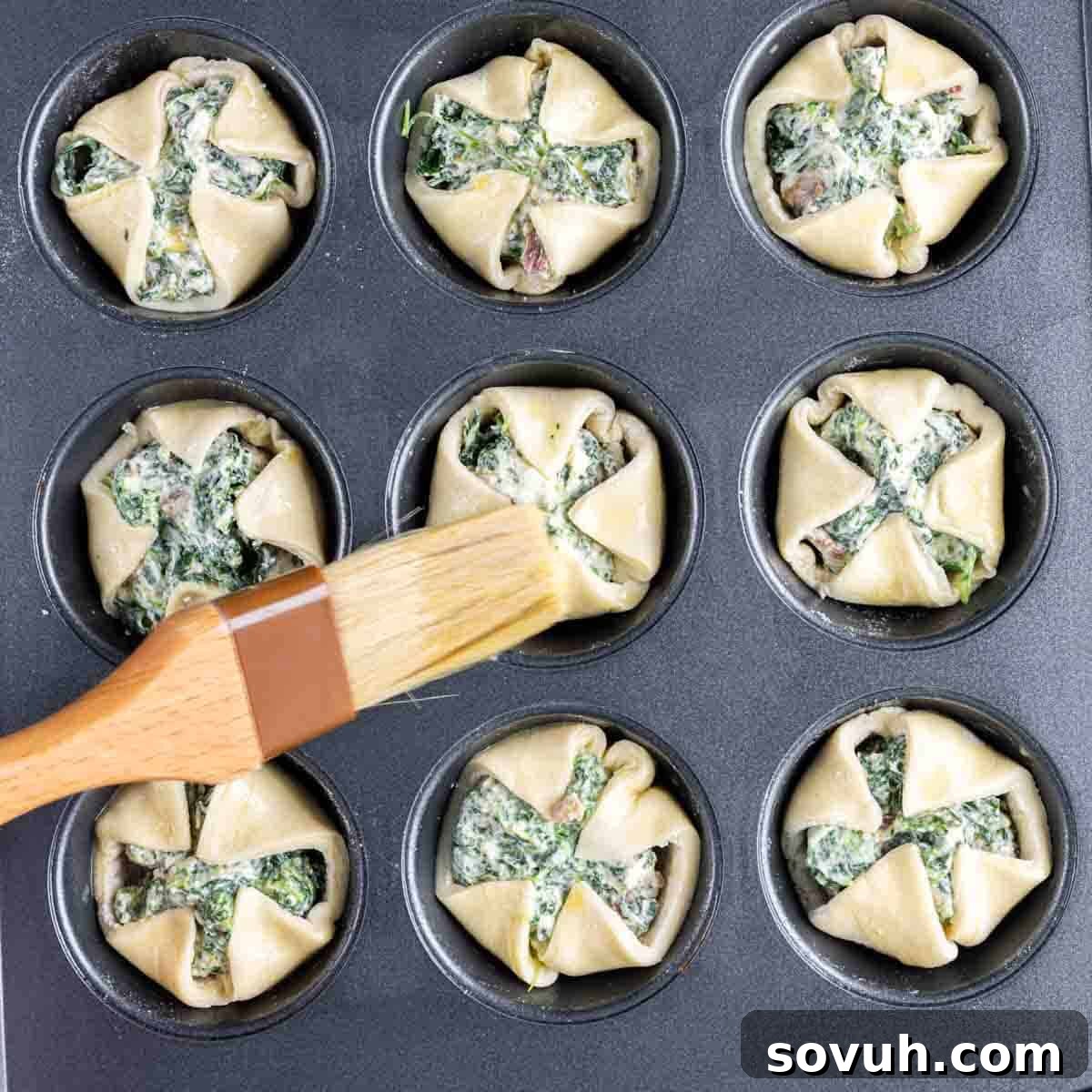 A muffin tin generously filled with spinach puff pastry cups, each overflowing with the savory spinach and bacon mixture.