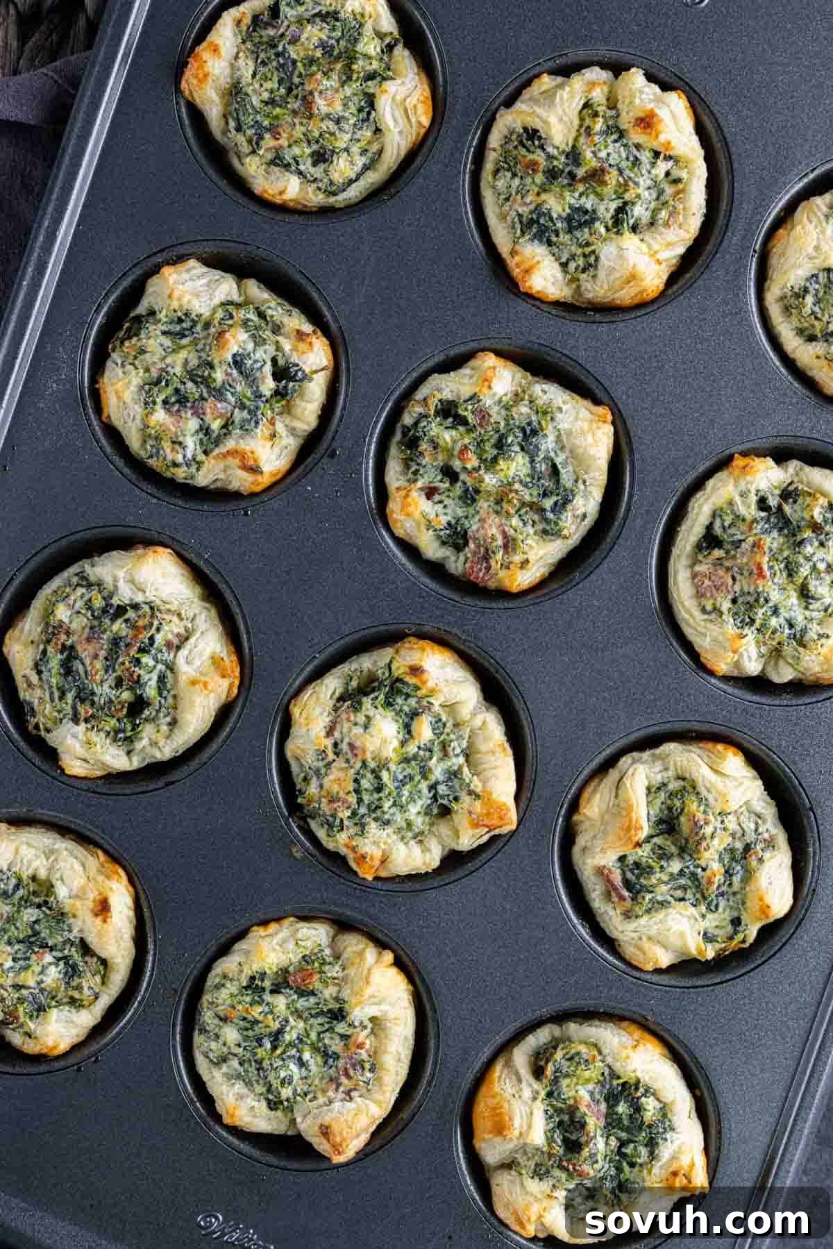 A muffin tin filled with unbaked spinach puffs, brushed with egg wash and ready to go into the oven.