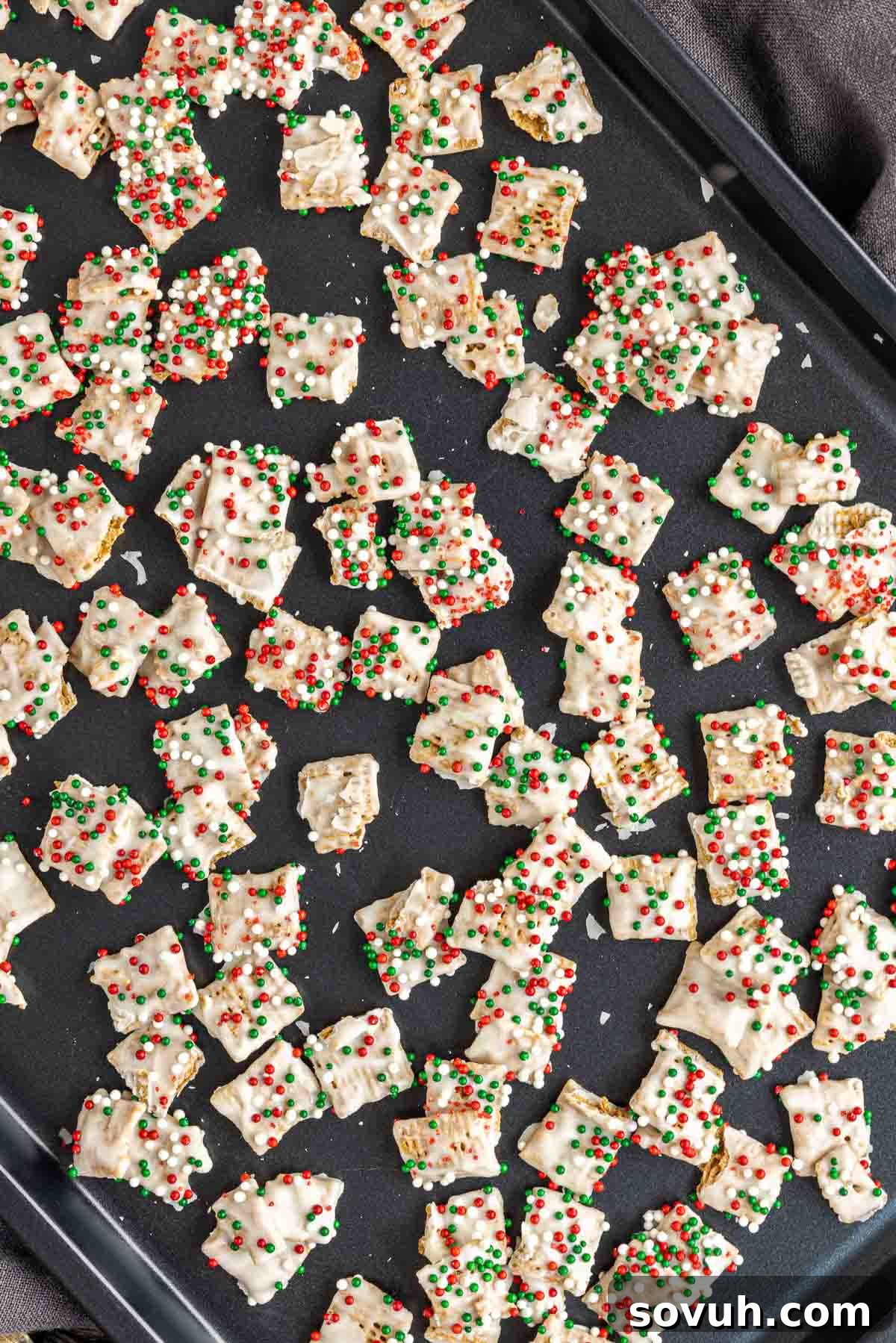 Close up of chocolate-covered rice Chex cereal with Christmas sprinkles on parchment paper, spread out to cool.