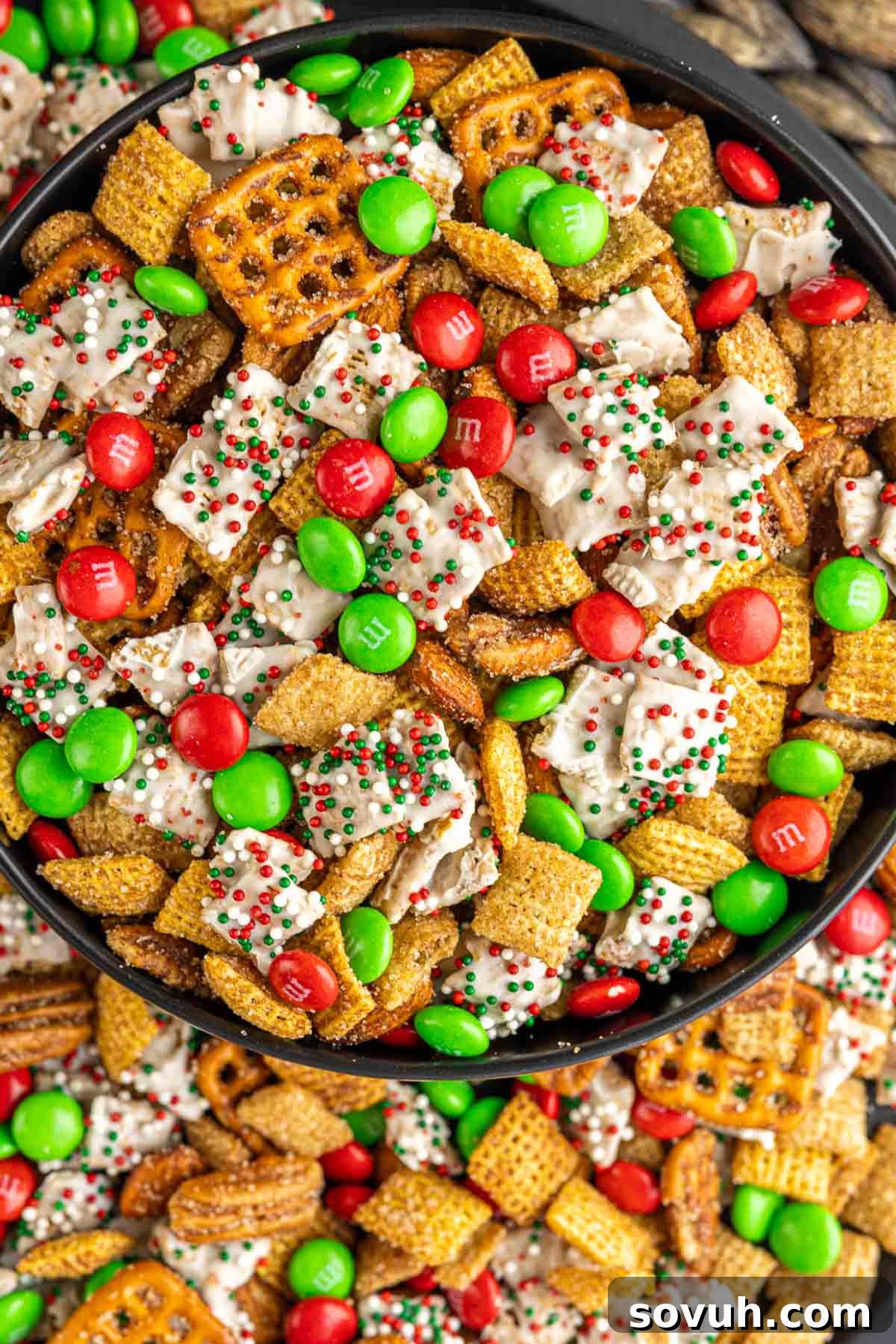 A black bowl brimming with the finished Christmas Chex Mix, showcasing a delightful mix of cereals, nuts, pretzels, and vibrant red and green M&Ms.