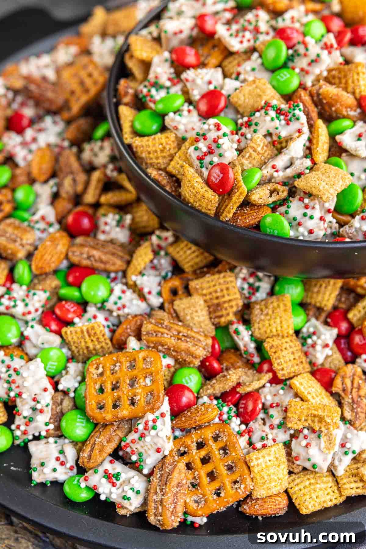 A close-up overhead shot of Christmas Chex Mix, showing cinnamon sugar Chex, white chocolate Chex with sprinkles, mini pretzels, and red and green M&Ms tossed together.