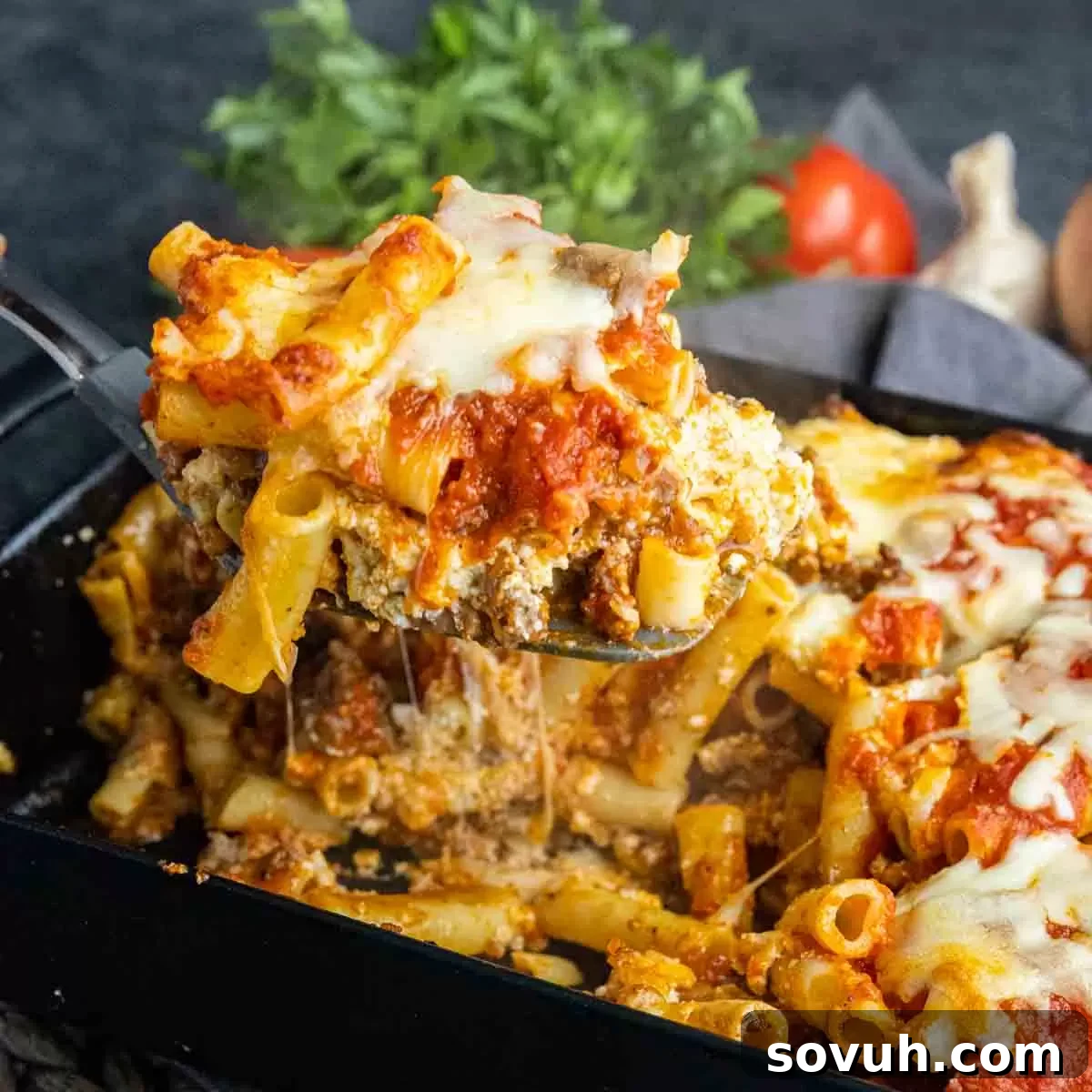 Serving a generous portion of Sausage Baked Ziti with steam rising, showcasing its rich layers of pasta, meat sauce, and melted cheese.