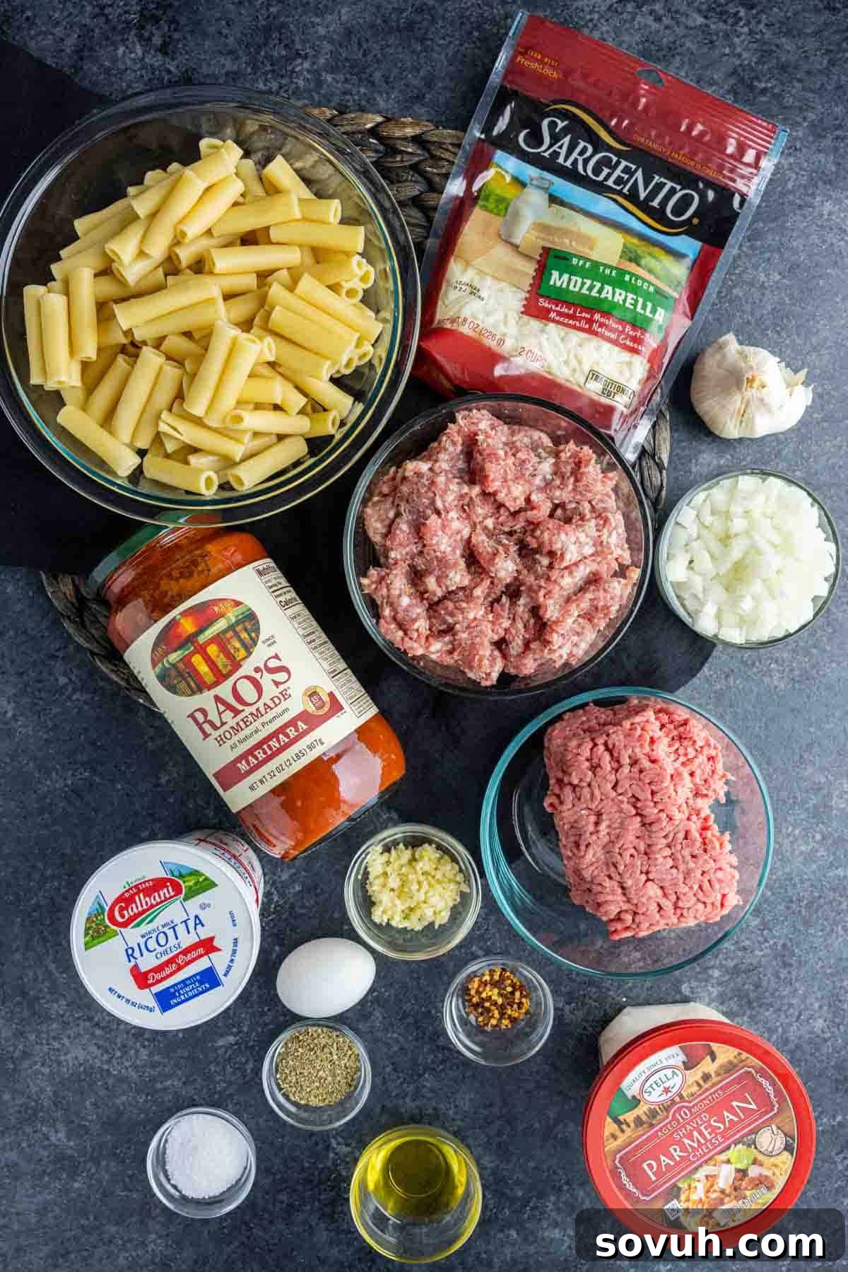 A vibrant display of fresh ingredients for Sausage Baked Ziti, including ziti pasta, ground Italian sausage, ground beef, fresh onions, garlic, and a variety of cheeses.
