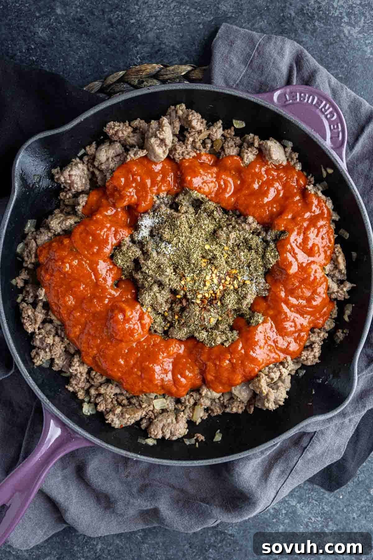 A large skillet containing the rich meat sauce for Sausage Baked Ziti, with pasta being added and stirred in to coat evenly.