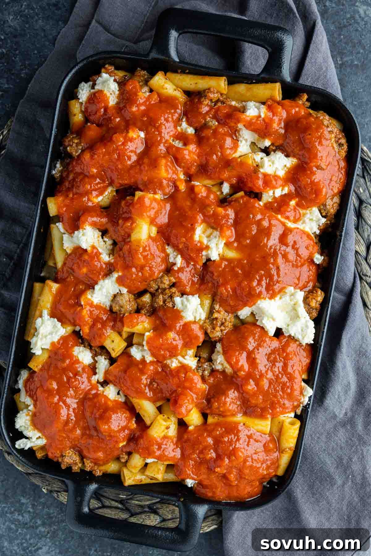 Sausage Baked Ziti in a casserole dish, topped with generous amounts of sauce before baking, showing the rich texture.