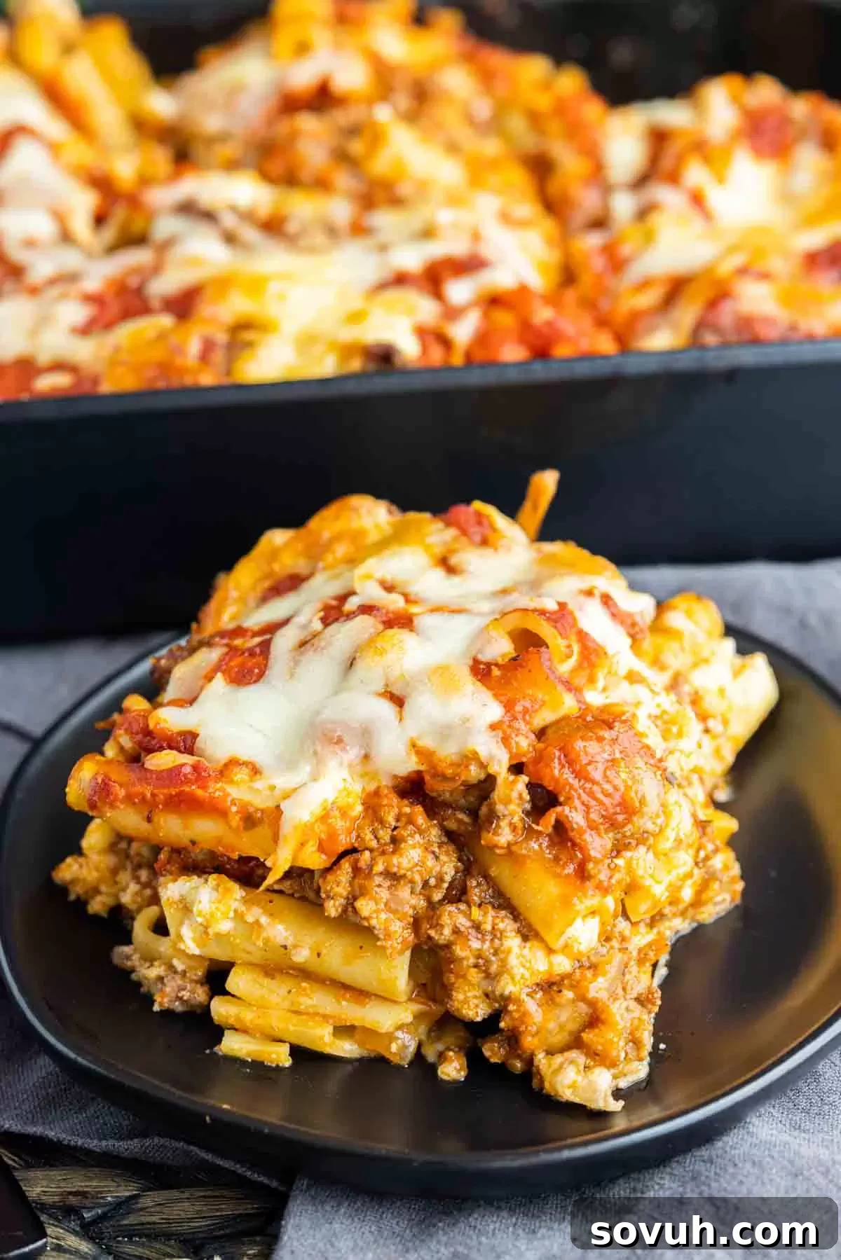 A perfectly portioned slice of Sausage Baked Ziti on a black plate, revealing the layers of pasta, rich meat sauce, and creamy cheese.