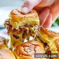 A hand pulling a single Bacon Cheeseburger Slider from a baking dish