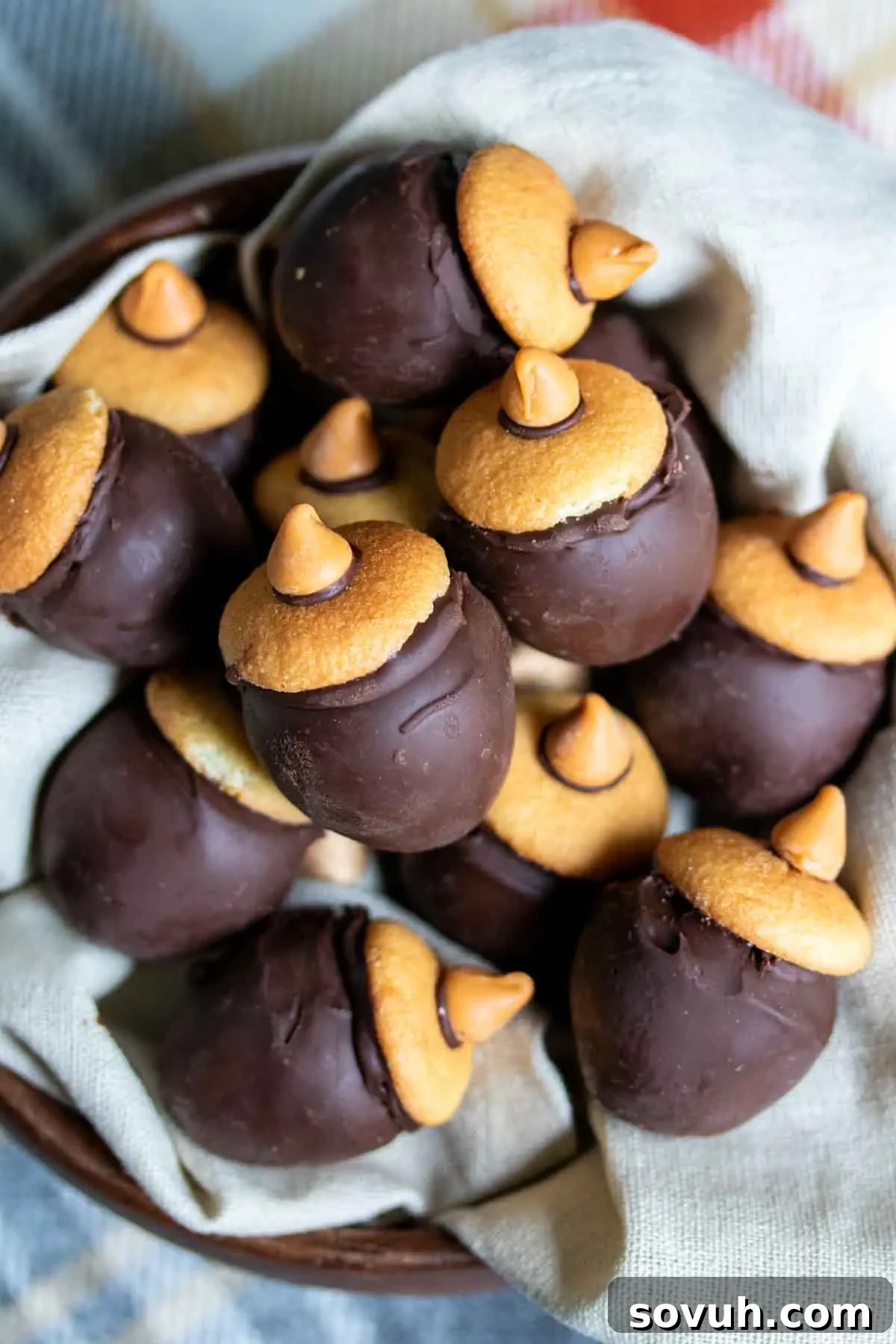 A bowl containing chocolate acorn-shaped treats with cookies and chocolate chips on a cloth napkin.
