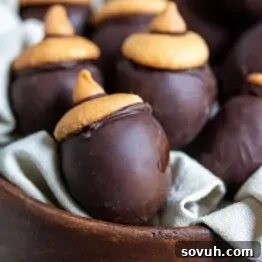 Close-up of chocolate acorn-shaped treats with cookie tops in a wooden bowl lined with fabric.