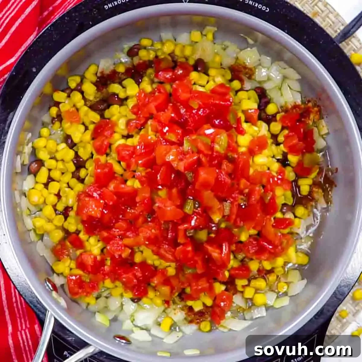 A pot containing a mix of diced onions, corn, black beans, and chopped red tomatoes, viewed from above to make filling for Chicken Tortilla Casserole