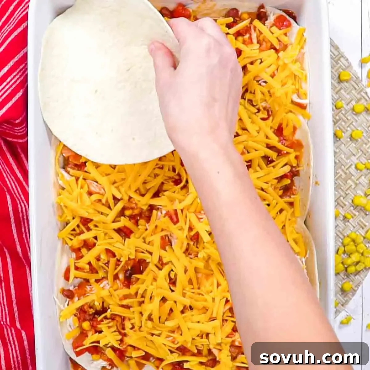 A person's hand placing a round dough layer on top of a Chicken Tortilla Casserole filled with cheese, beans, and corn.