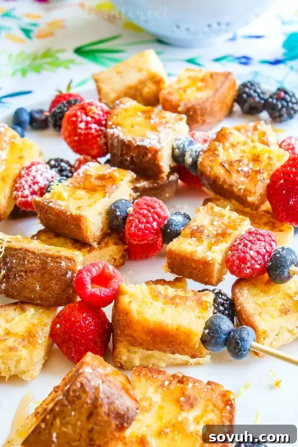 Lemon pound cake french toast with fresh raspberries and blueberries drizzled with syrup, served on a white plate