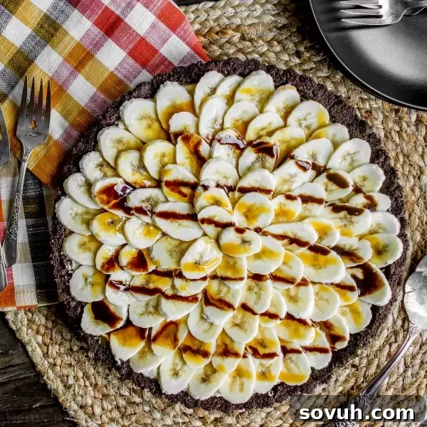 An appetizing overhead view of a Banana Fluffernutter Pie, showing layers of creamy peanut butter, fluffy marshmallow, and fresh banana slices, drizzled with chocolate and caramel.