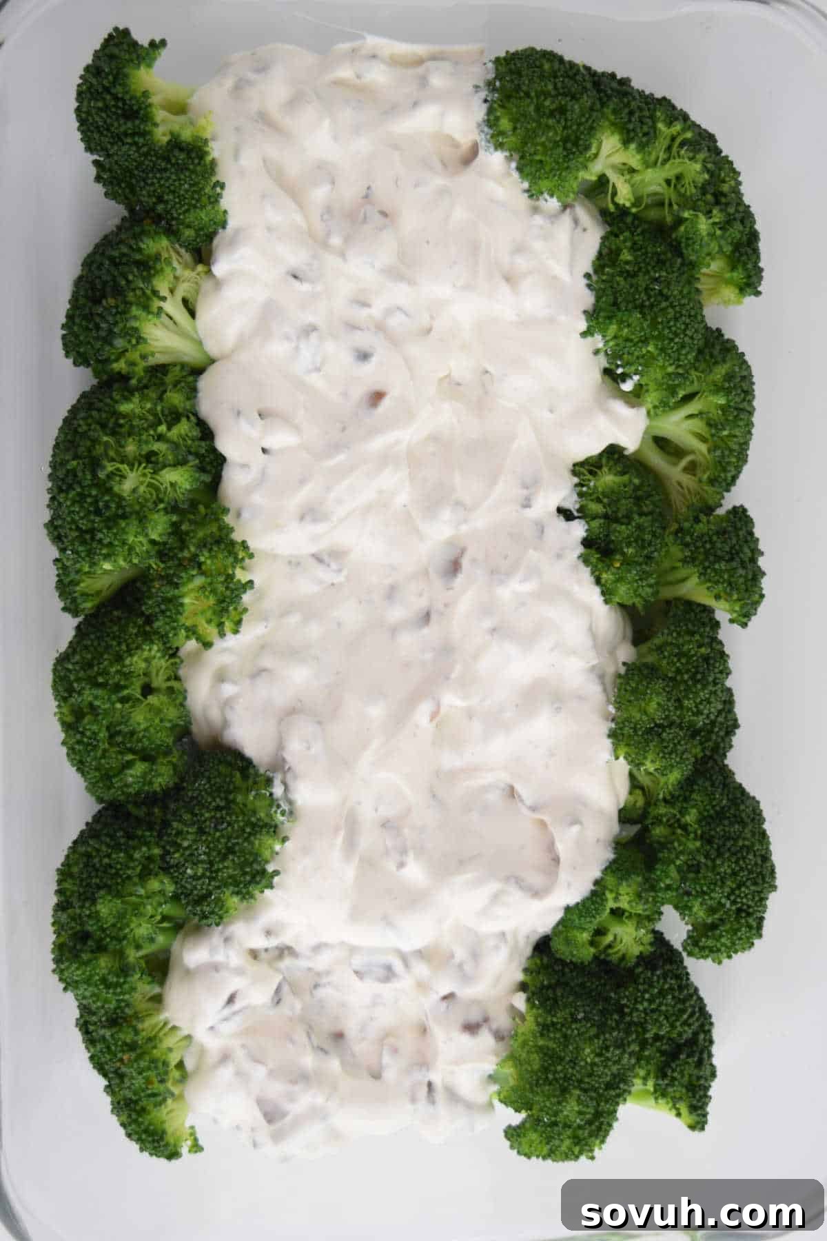 Mushroom soup and sour cream mixture being poured over broccoli in a casserole dish