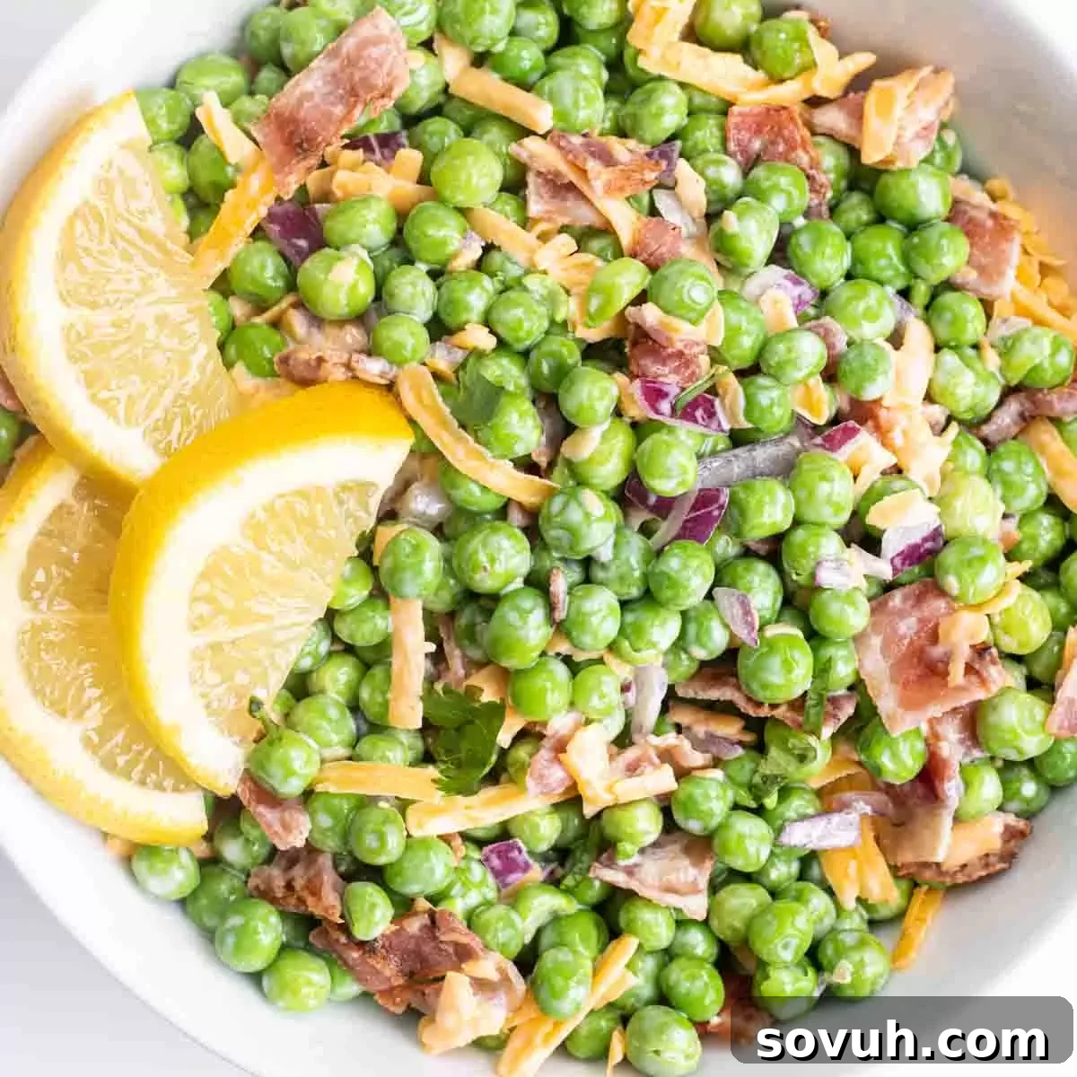 Velvety Spring Pea Salad 2 a white bowl of english pea salad garnished with fresh lemon slices
