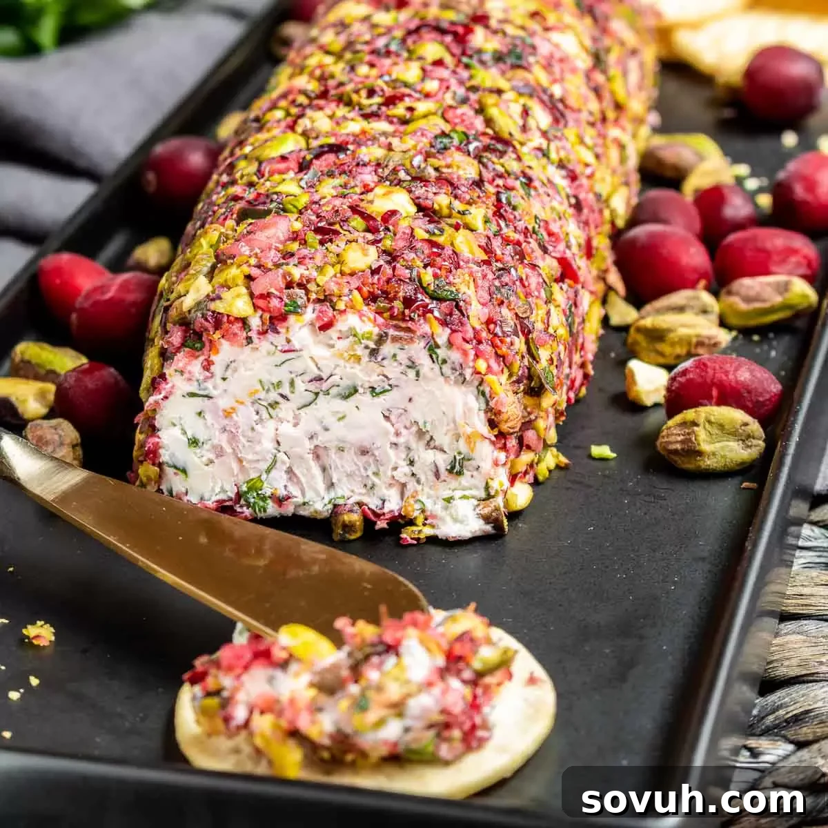 Elegant Cranberry Goat Cheese Log on a black platter, garnished with fresh cranberries and rosemary, ready to serve.