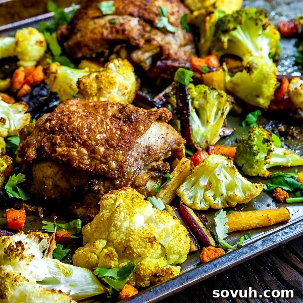 Close-up of crispy curried chicken thighs and colorful roasted vegetables on a sheet pan