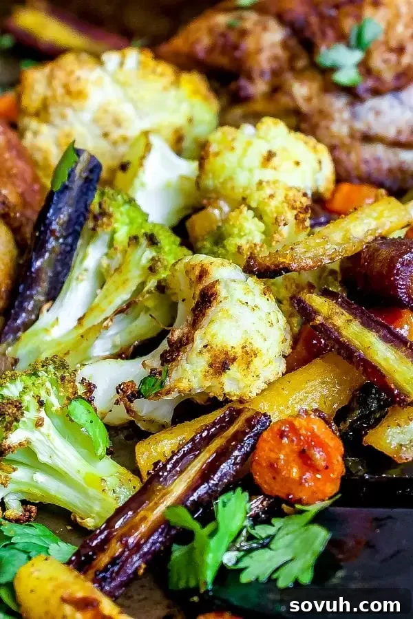 Roasted curried vegetables on a baking sheet, featuring green and white cauliflower and rainbow carrots