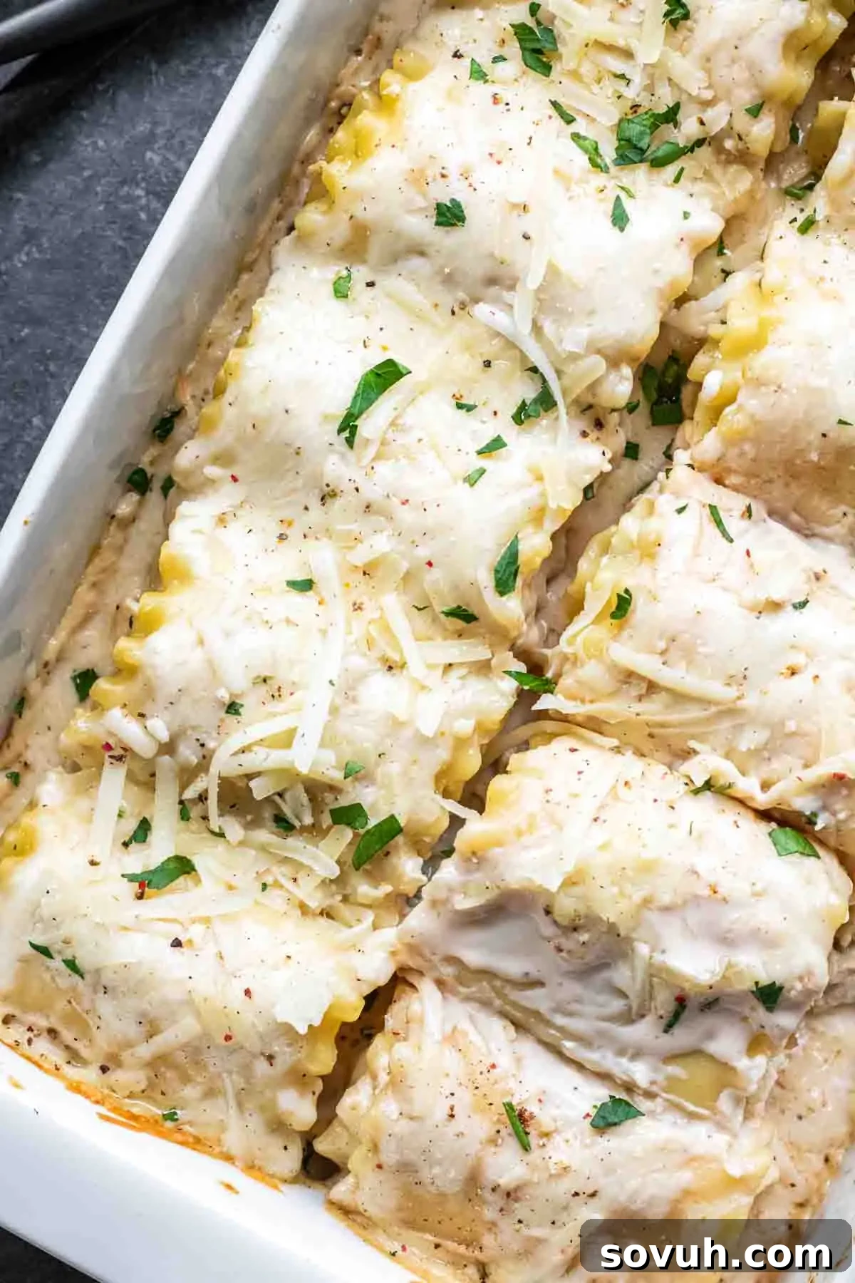Lasagna topped with melted cheese and garnished with fresh herbs in a white baking dish.