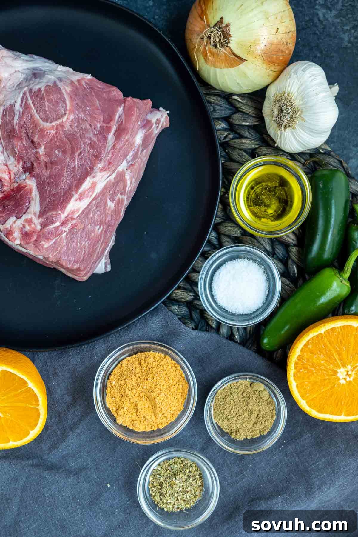 A selection of fresh ingredients for Slow Cooker Pulled Pork Carnitas, including pork shoulder, onions, garlic, jalapenos, and an orange.