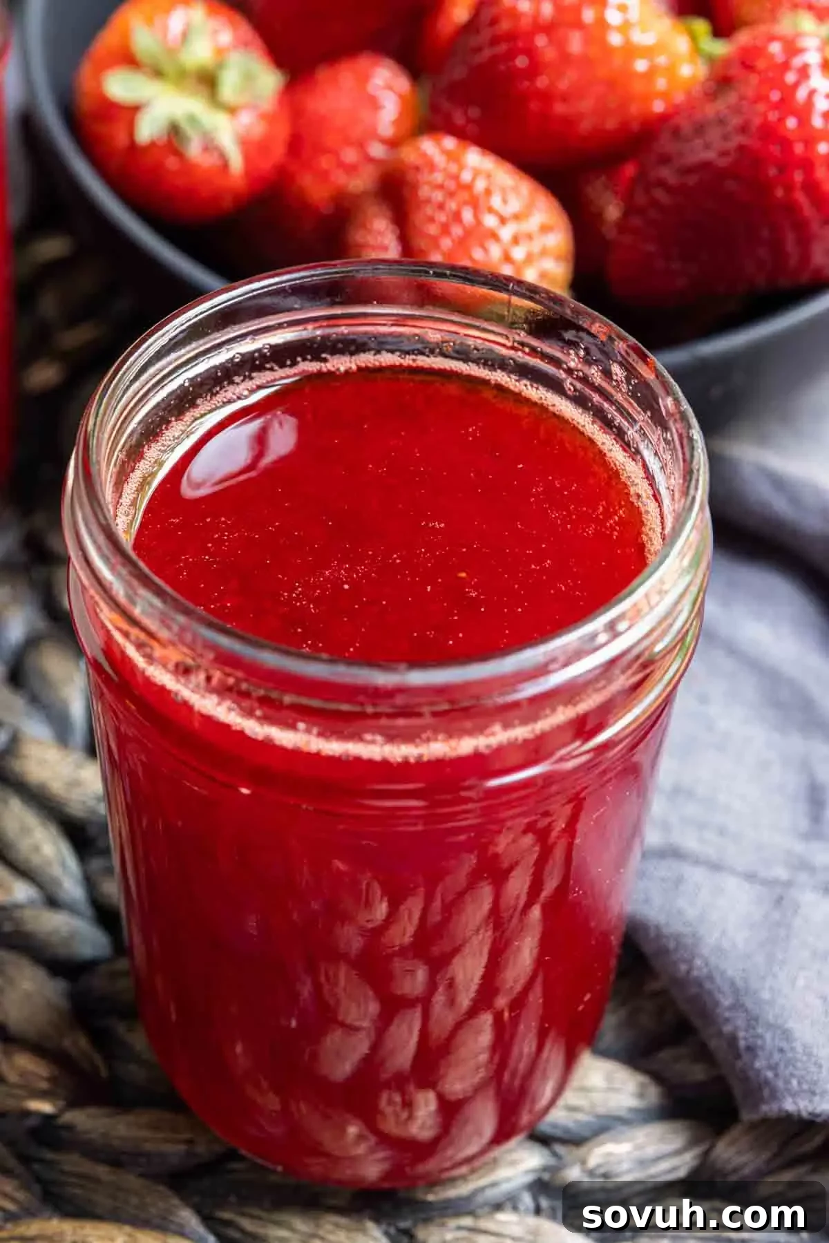 Strawberry Coulis in a glass jar with a bowl of fresh strawberries in the background