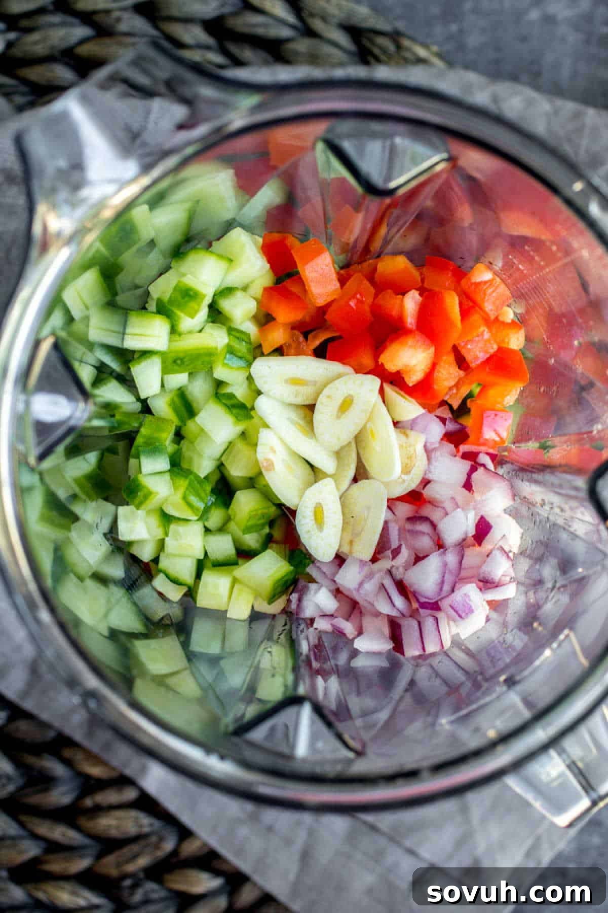 Fresh ingredients for Gazpacho Soup, including tomatoes, cucumbers, bell peppers, and onion, being added into a blender, illustrating the simple preparation process.