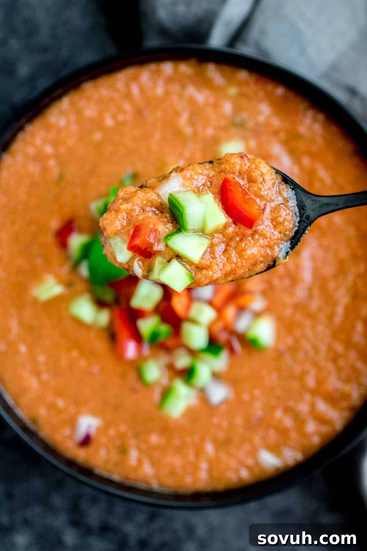 Close-up shot of Gazpacho Soup on a spoon, highlighting its smooth texture and vibrant red color.