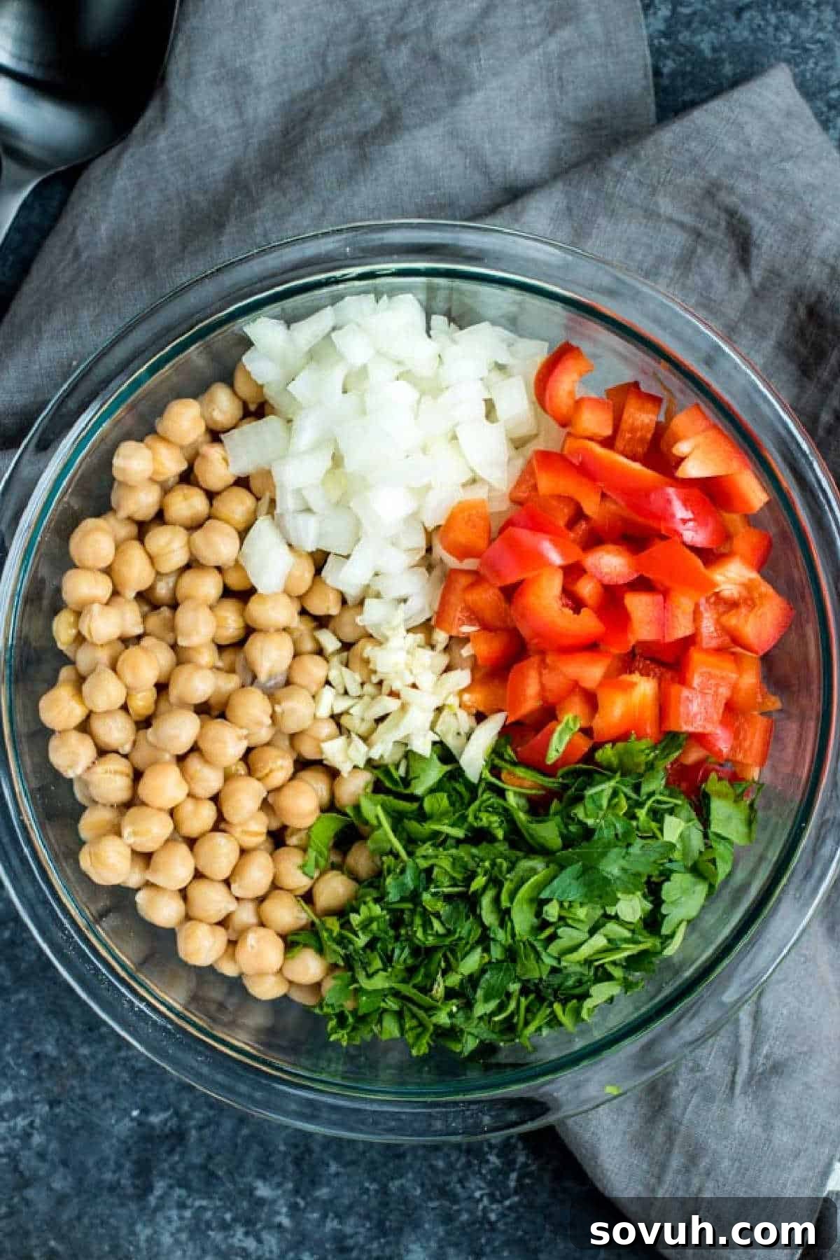 Fresh ingredients laid out on a wooden board for Mediterranean Chickpea Salad preparation: chickpeas, bell peppers, onions, garlic, and parsley