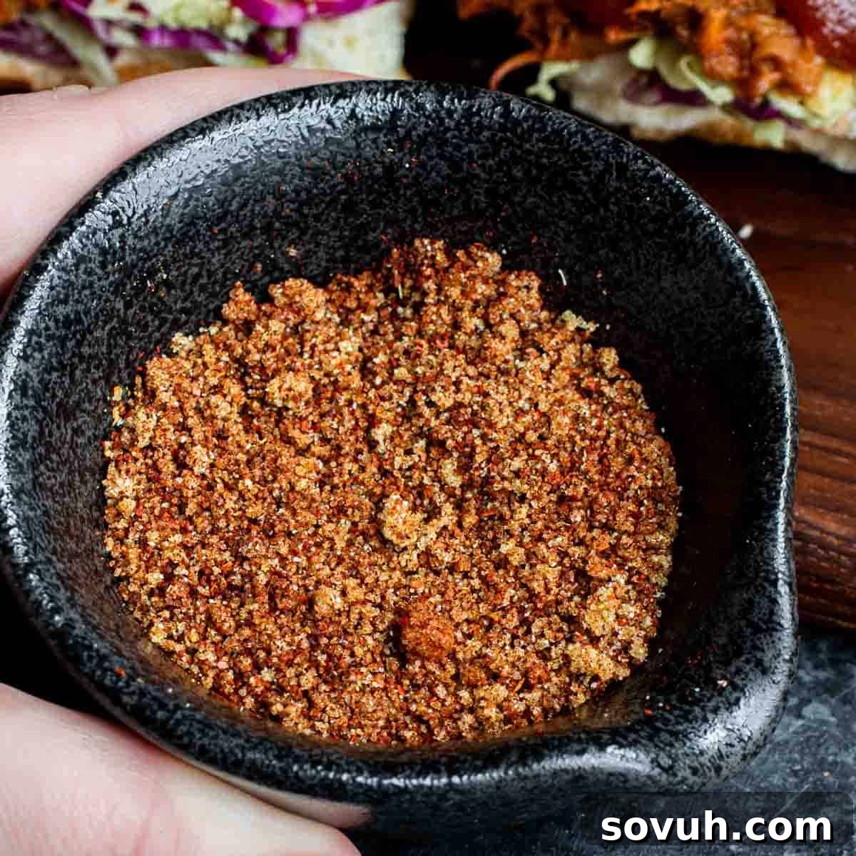 The Ultimate Memphis Dry Rub 2 A hand holding a black bowl filled with a homemade Memphis Dry Rub, ready to be applied to meat.