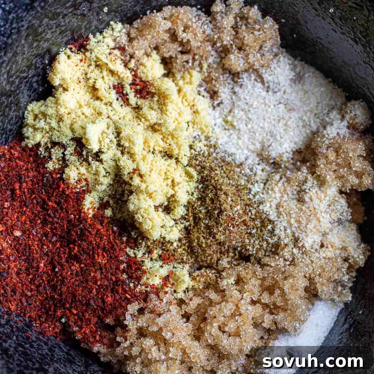 The Ultimate Memphis Dry Rub 3 A mix of various ground spices and seasonings, including red chili powder, brown sugar, ginger, and salt, artfully arranged in a dark bowl, ready to be blended into a Memphis Dry Rub.