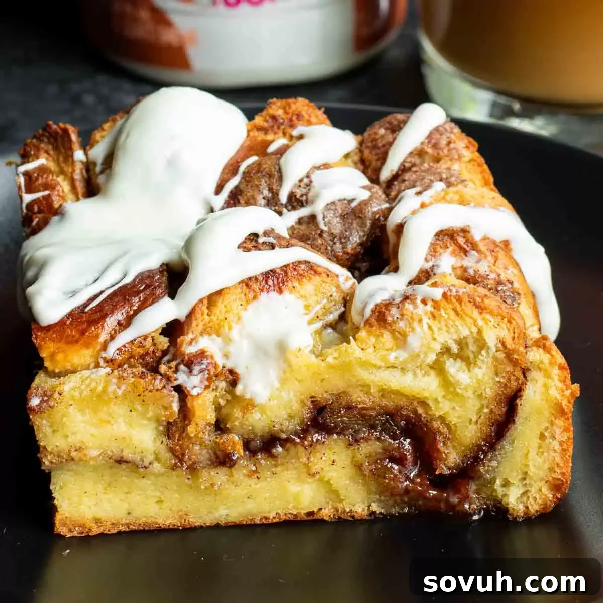 A delectable slice of Cinnamon Roll French Toast Casserole, generously topped with cream cheese icing, served on a white plate, ready to be enjoyed.