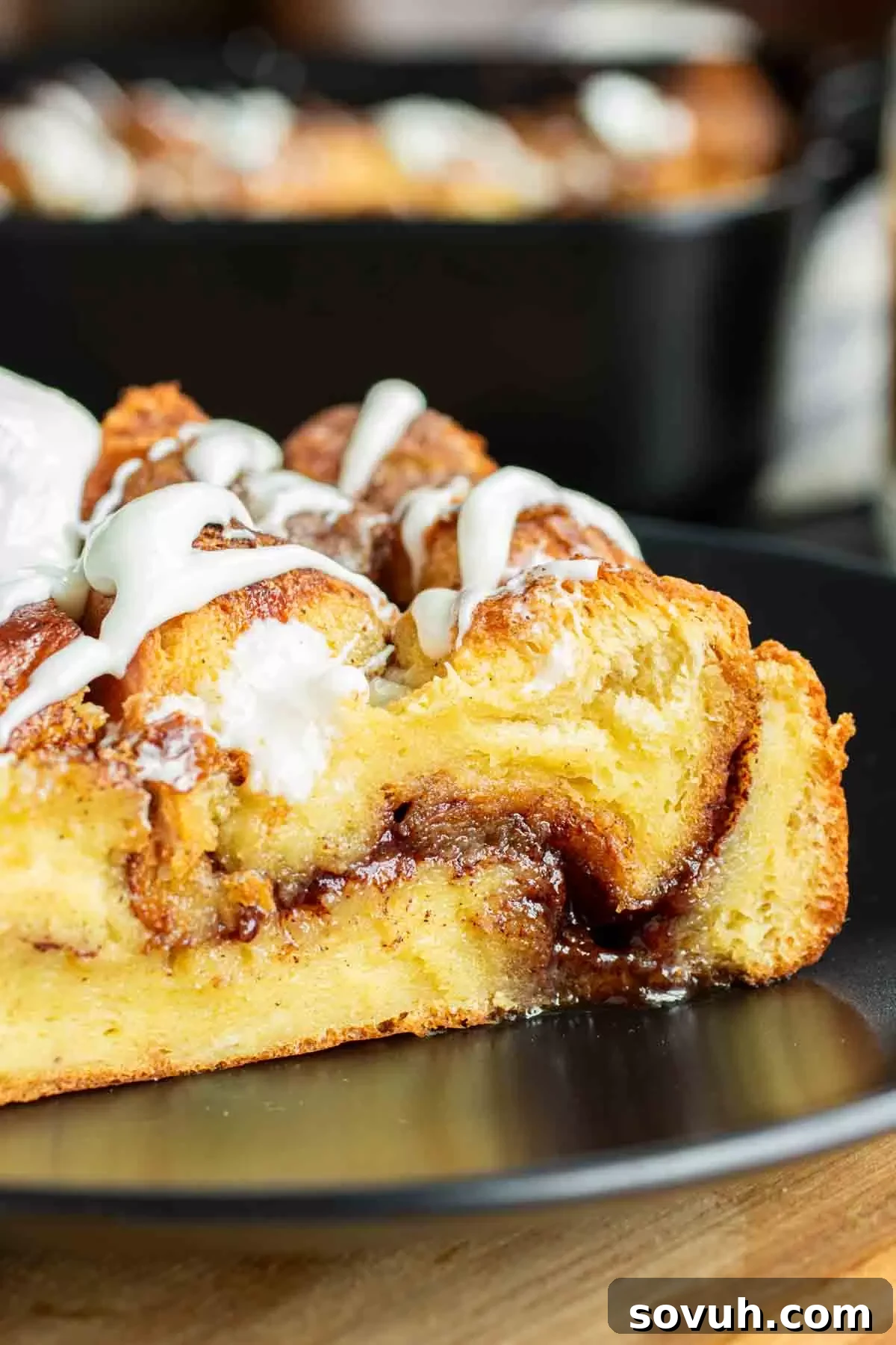 A perfectly portioned slice of Cinnamon Roll French Toast Casserole, glistening with cream cheese icing, artfully presented on a clean white plate, ready for a delicious breakfast or brunch.