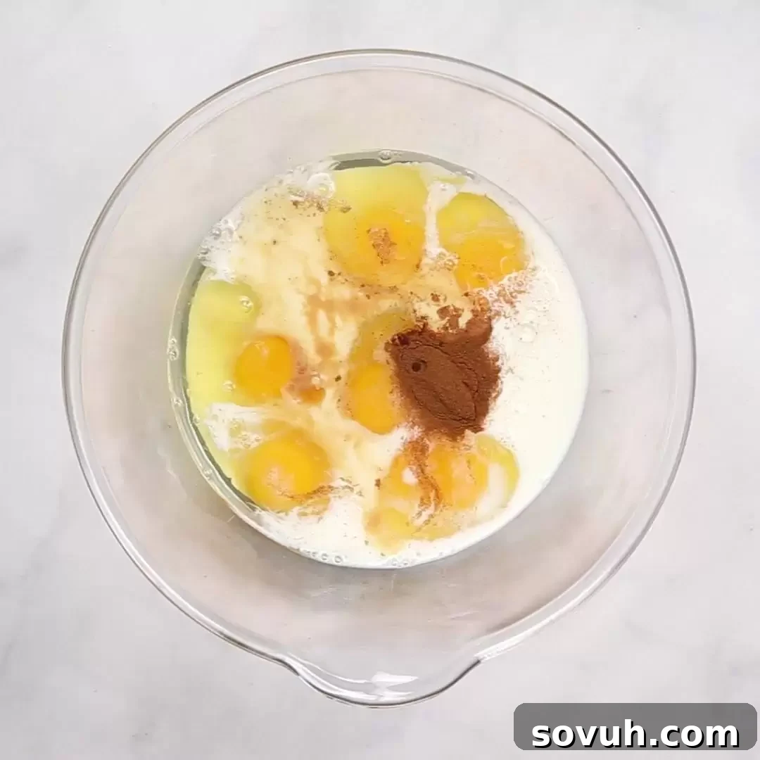A clear glass bowl filled with the creamy French toast custard mixture, consisting of eggs, milk, vanilla creamer, and a touch of salt and cinnamon, ready to be whisked.