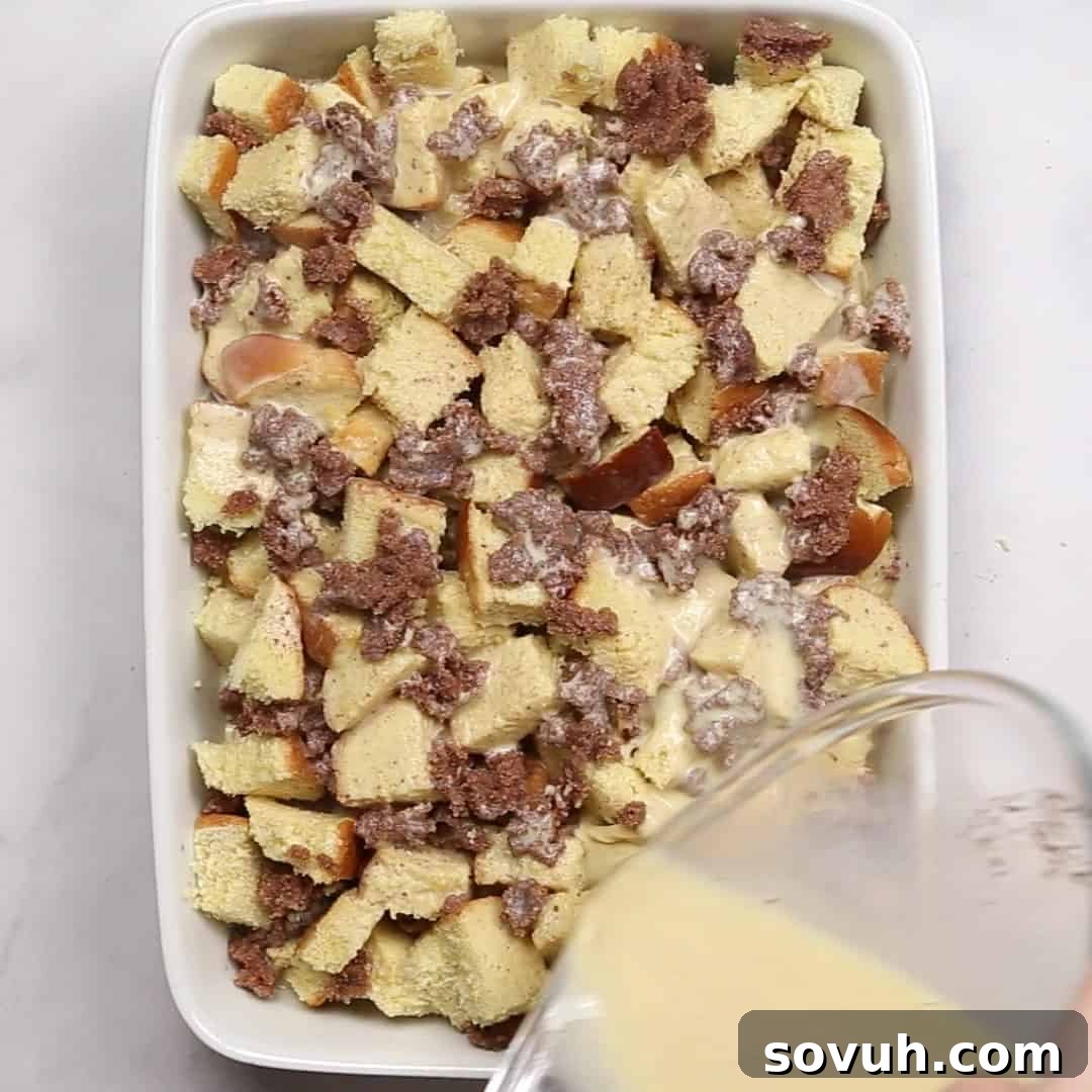 The creamy egg and milk mixture being poured evenly over the layers of bread and cinnamon-sugar in a baking dish, ensuring every piece is well-moistened for an overnight soak.