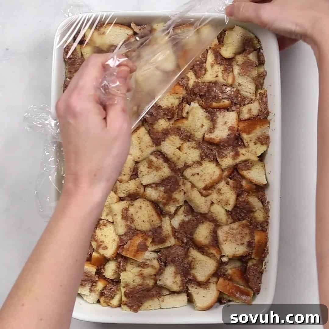 A golden-brown slice of freshly baked Cinnamon Roll French Toast Casserole being gently lifted from the baking dish with a spatula, steam rising, highlighting its readiness.