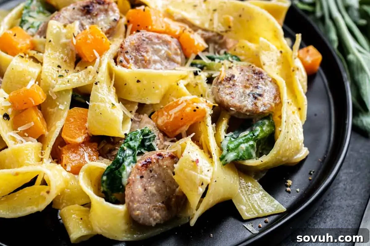 Creamy Sausage Pasta with Butternut Squash – Easy Weeknight Dinner Close-up of a pasta dish with sliced sausage, spinach, and diced squash, garnished with grated cheese and black pepper on a black plate.