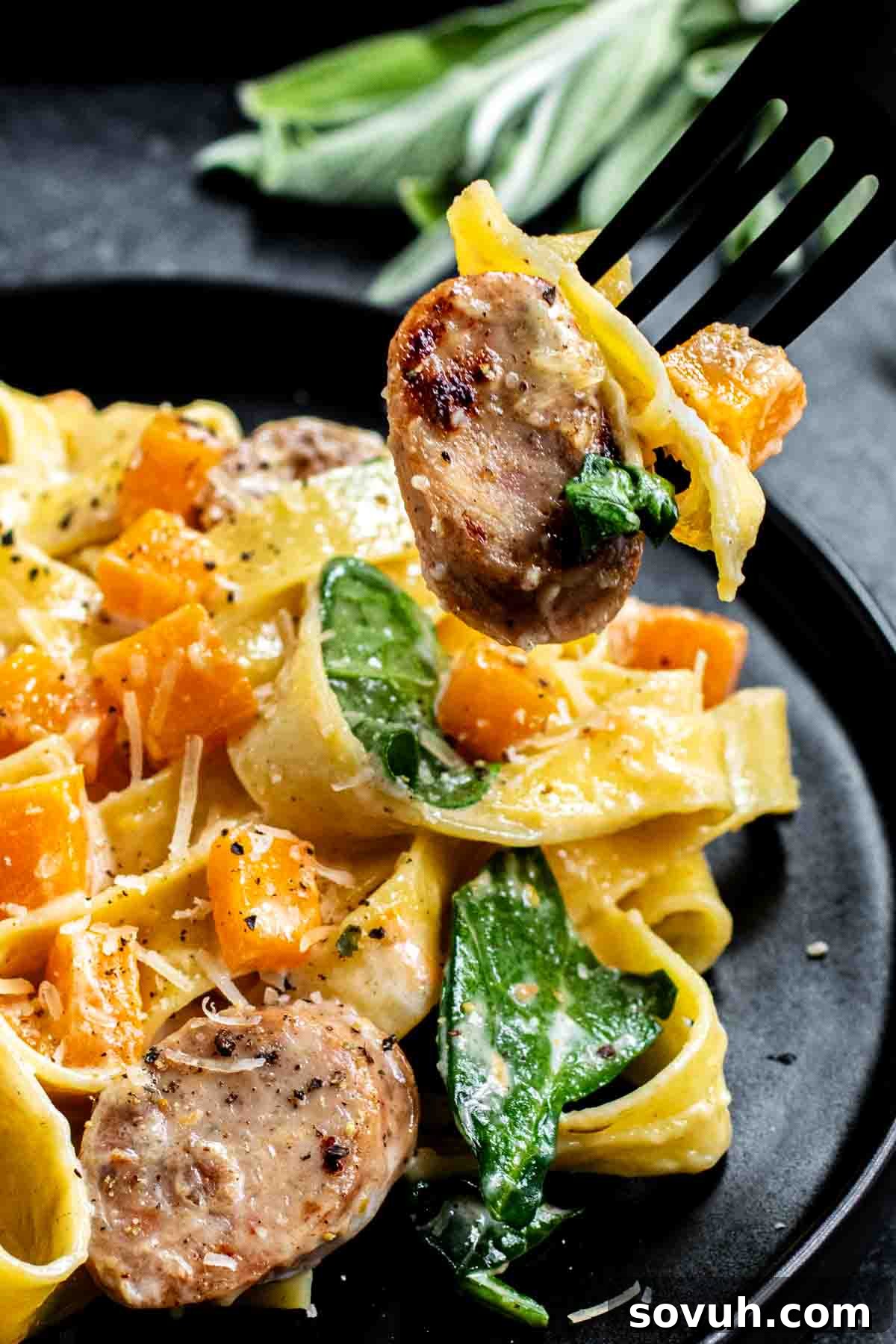 Serving of Creamy Butternut Squash Pasta Fork holding pasta, sausage slice, spinach, and diced squash over a plate of creamy pasta.