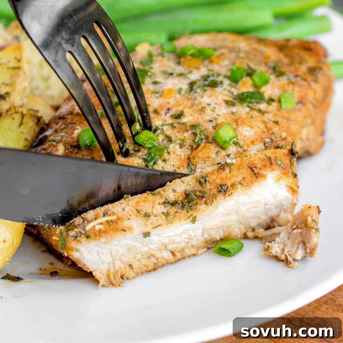 Slicing into juicy Baked Ranch Pork Chops with a knife, revealing the tender interior