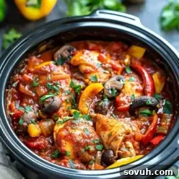A close-up of a Slow Cooker Chicken Cacciatore, featuring chicken pieces, bell peppers, mushrooms, and tomato sauce, garnished with fresh herbs.