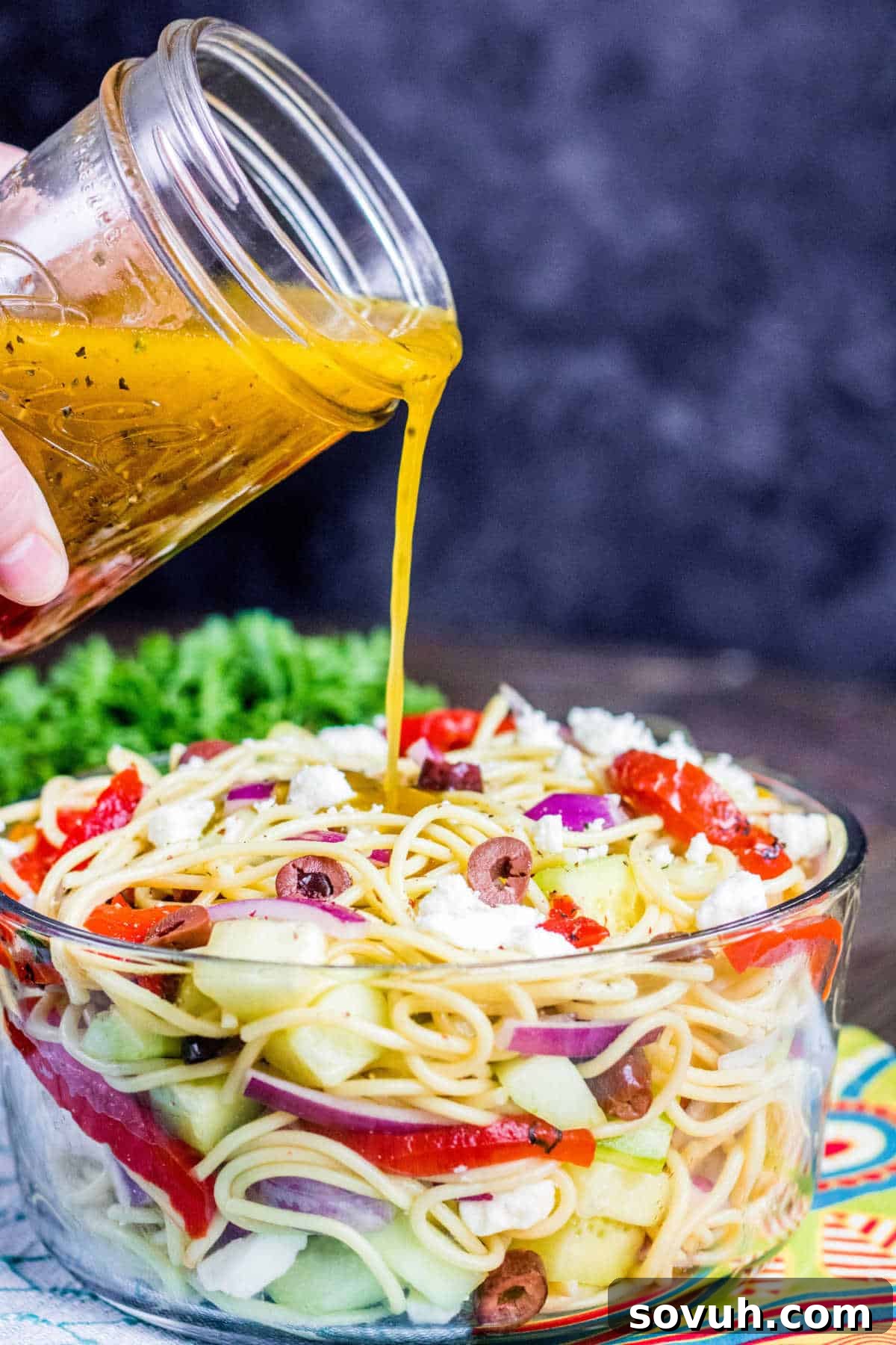 pouring dressing over Greek Spaghetti Salad