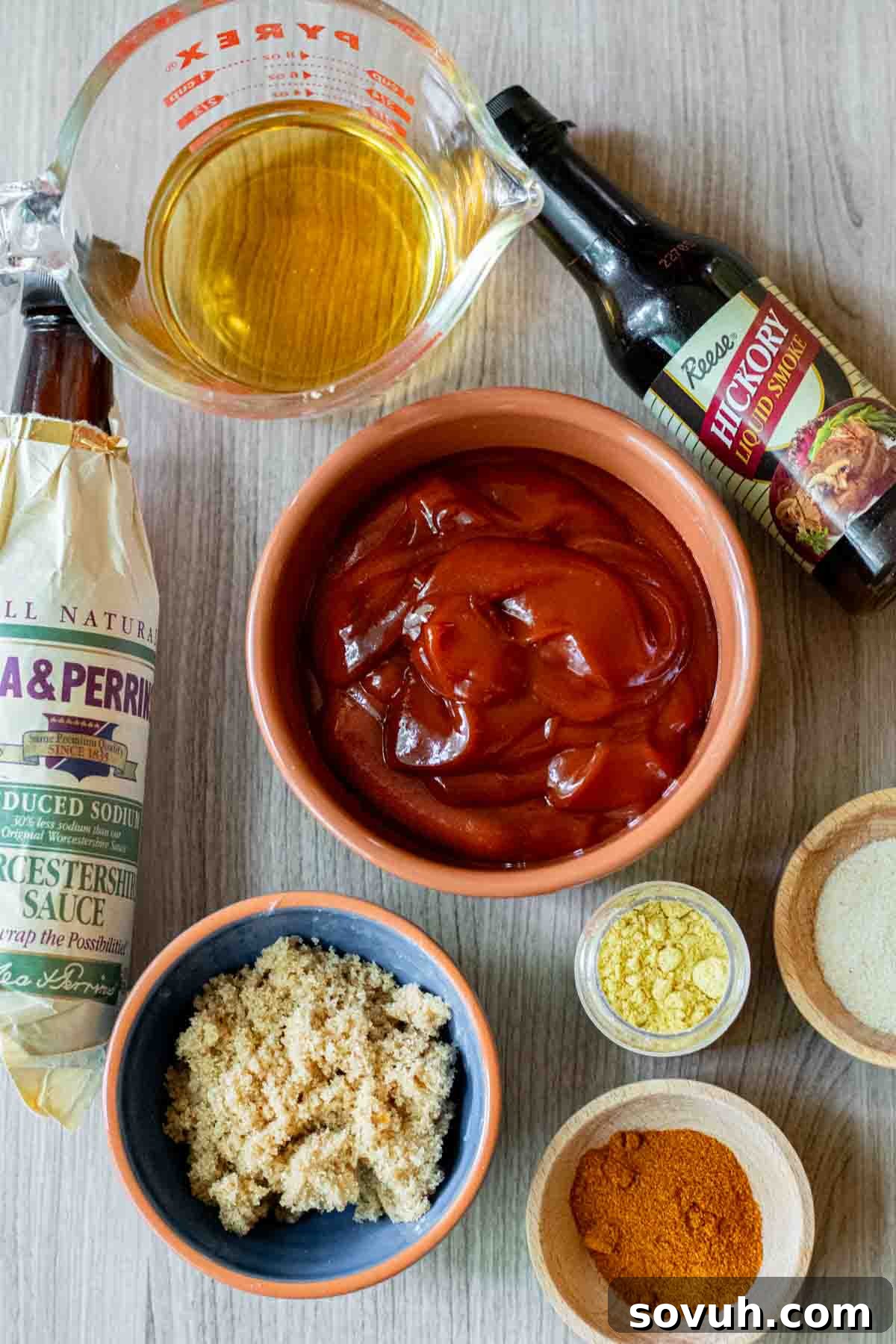 A selection of essential ingredients for homemade Memphis BBQ Sauce, including a bottle of ketchup, apple cider vinegar, brown sugar, Worcestershire sauce, and various spices, arranged on a rustic wooden table.