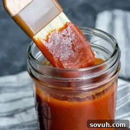 A brush applying Memphis BBQ Sauce from a jar on a textured dark background.