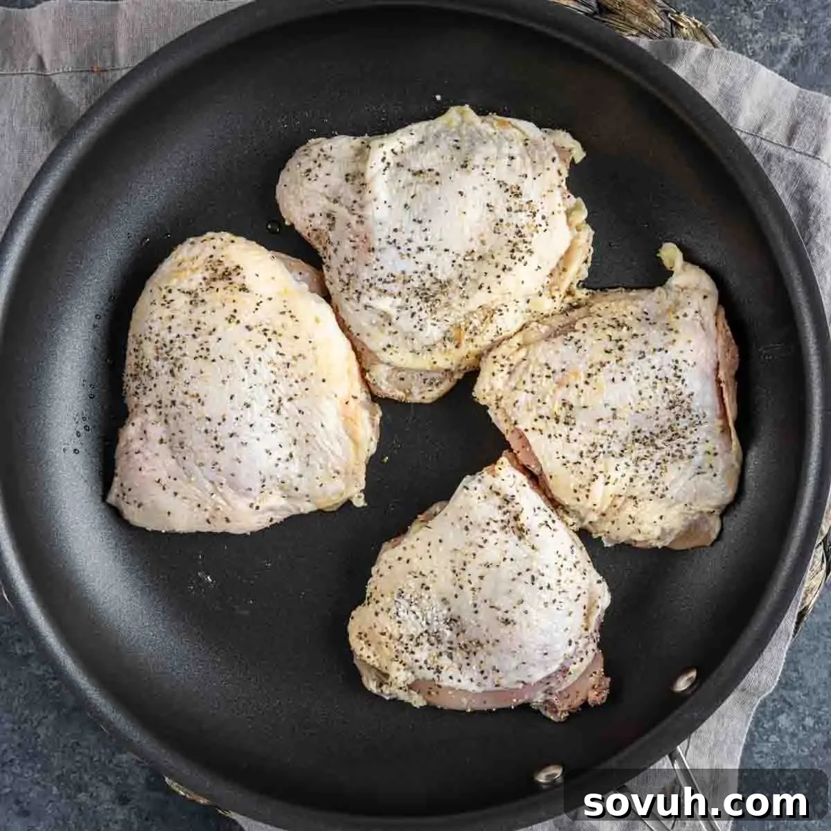Four seasoned chicken thighs being cooked in a large non-stick frying pan, their skins turning golden brown and crispy, for Parmesan Chicken Orzo.